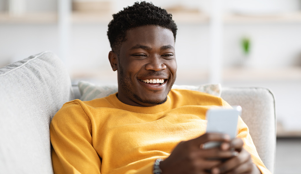 Un homme souriant regarde son téléphone portable allongé dans son canapé