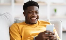 Un homme souriant regarde son téléphone portable allongé dans son canapé
