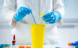 Deux mains gantées bleues mélangent du liquide dans un contenant jaune
